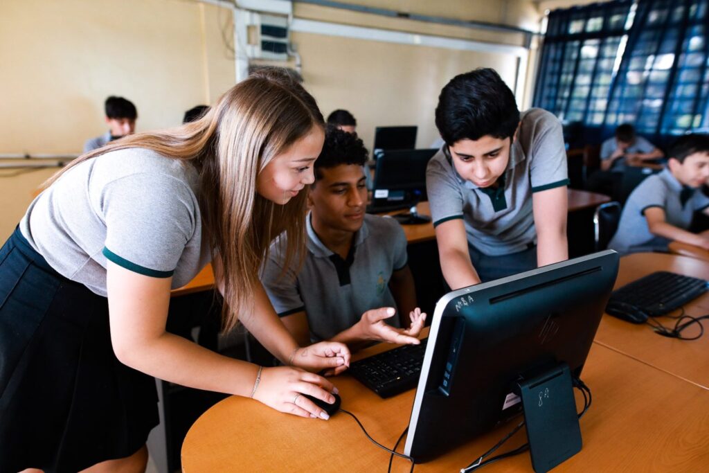 estudiantes al rededor de un computador en el aula webinar IACC directora Paulina Retamales